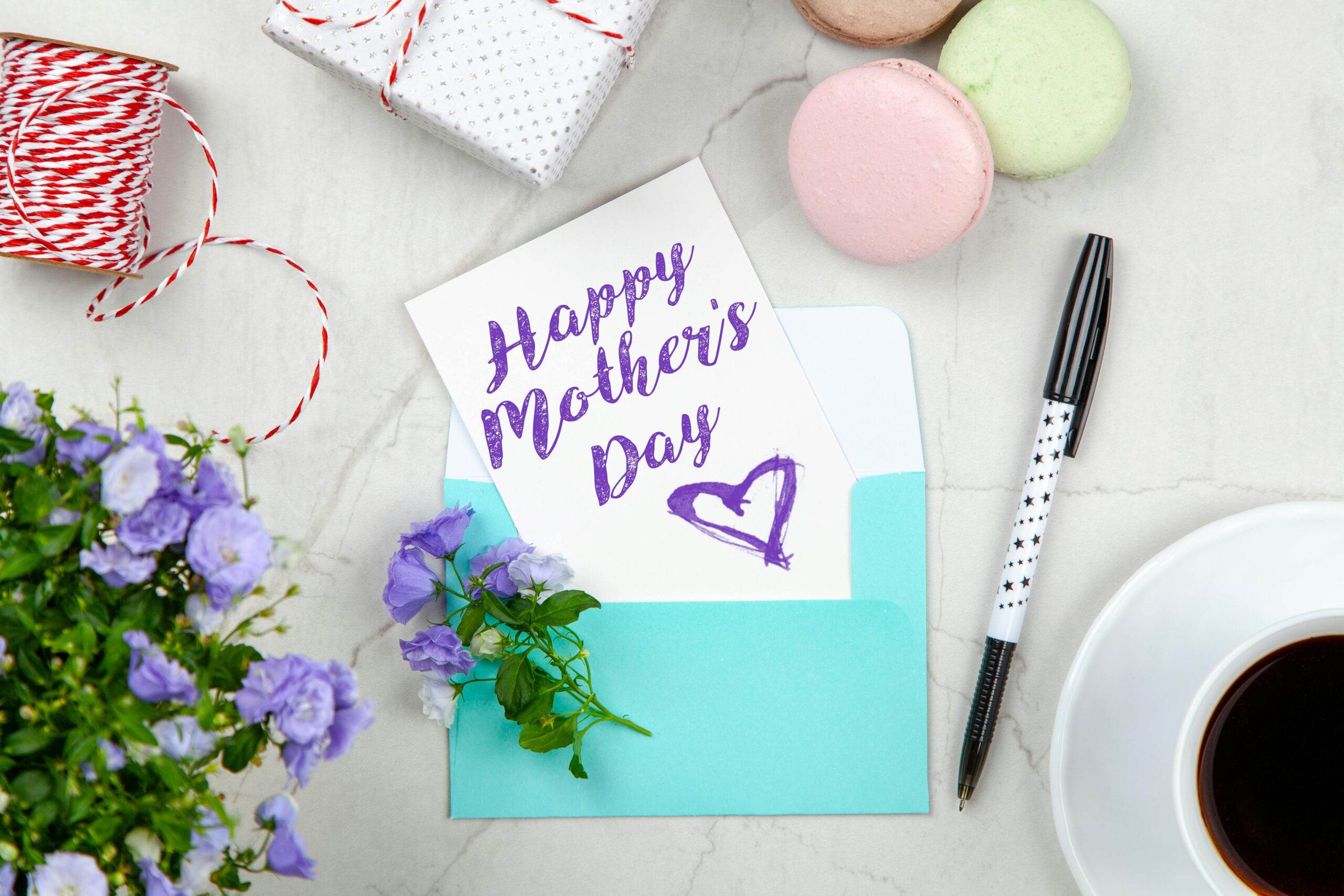 Creative Mother's Day card setup with flowers, coffee, and macarons on a marble table.