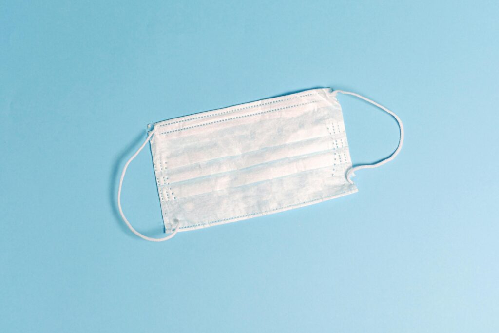 A disposable face mask lying on a light blue surface, symbolizing health protection.